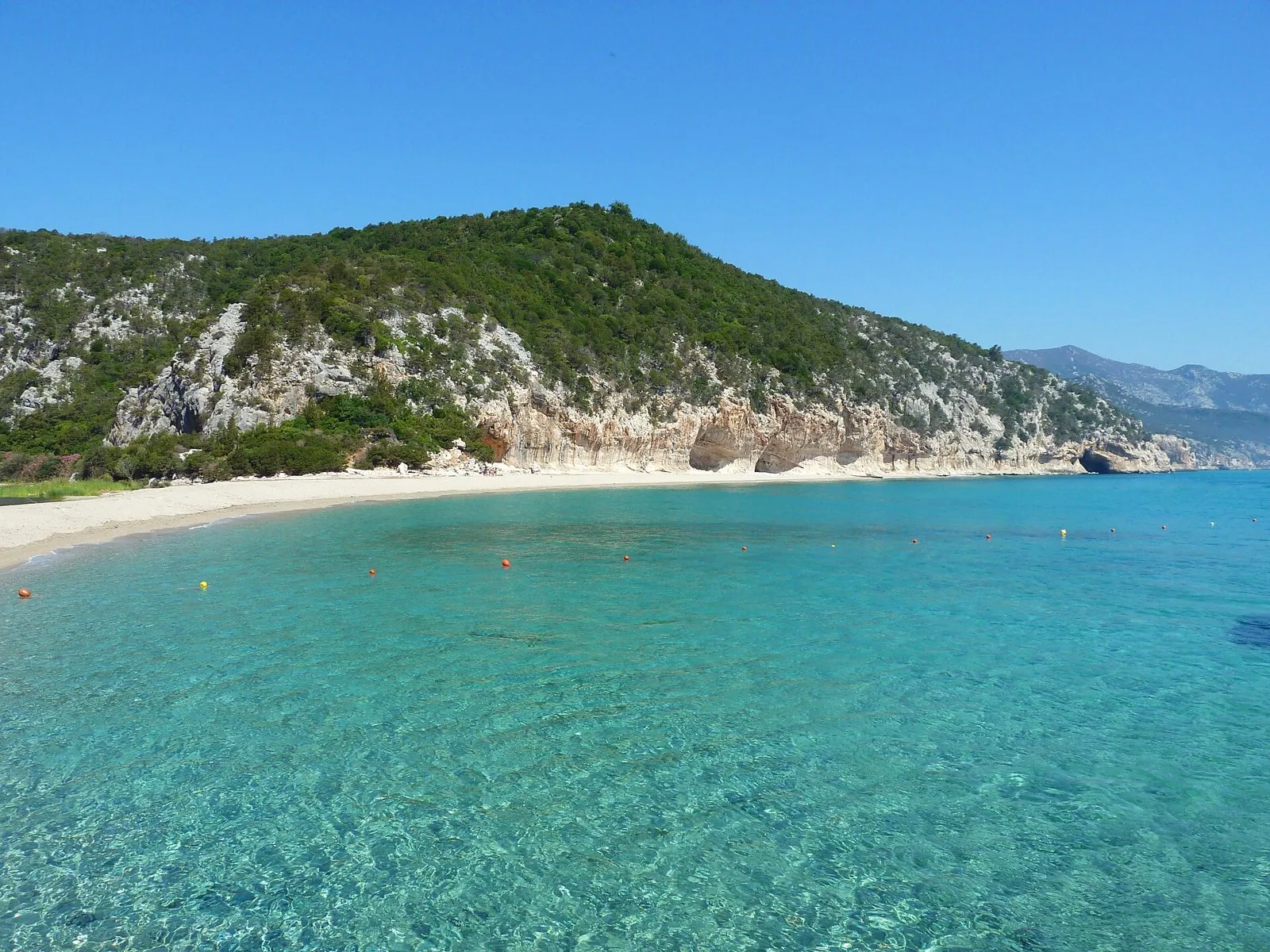 La spiaggia di Cala Luna con l'acqua turchese, la falesia calcarea con le grotte e il promontorio coperto di macchia