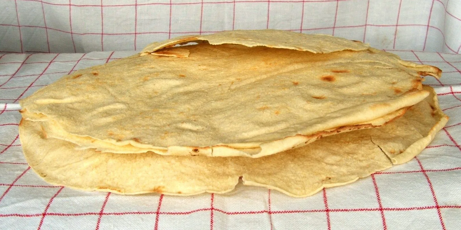 Fogli di pane carasau sovrapposti su una tovaglia a quadri bianca e rossa
