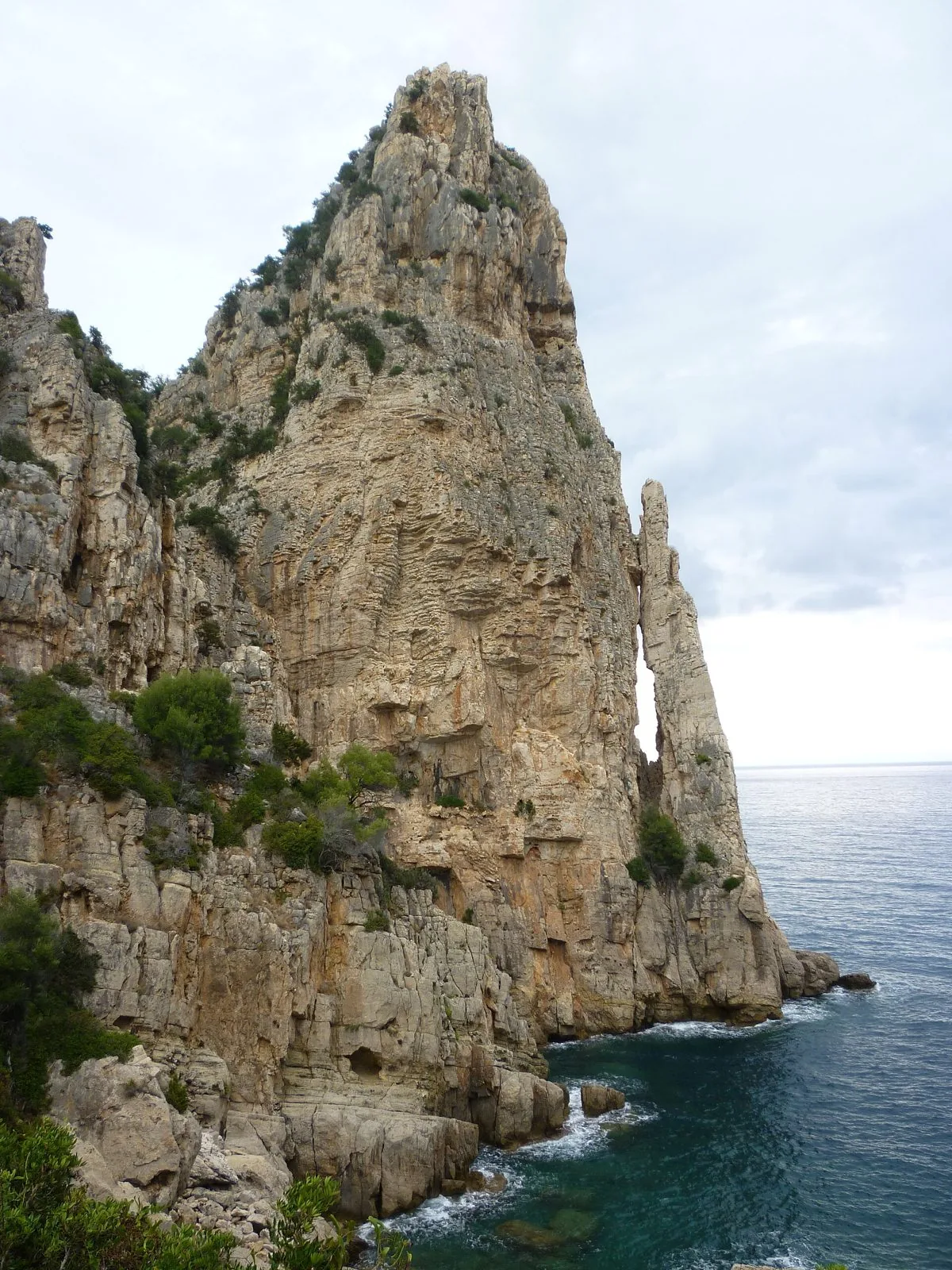 Il pinnacolo calcareo di Pedra Longa che si alza a picco sul mare, con la costa rocciosa e la macchia mediterranea